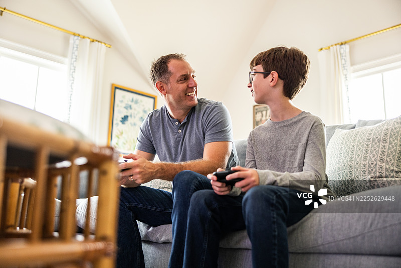父亲和儿子一起在沙发上玩电子游戏图片素材