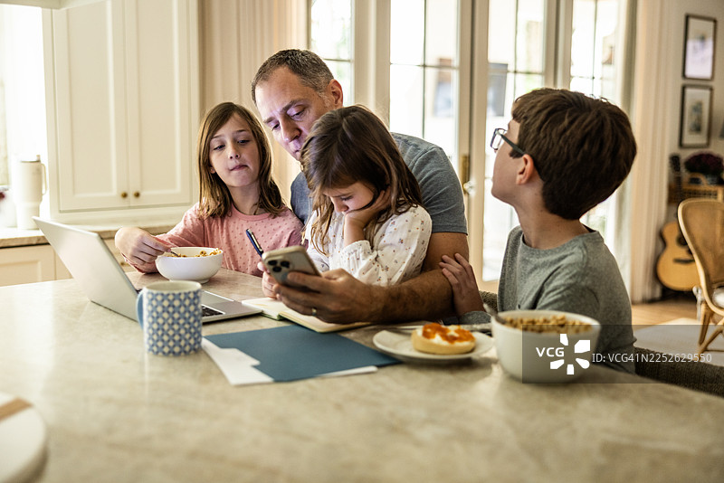 父亲在厨房里一边工作一边同时照顾三个年幼的孩子图片素材