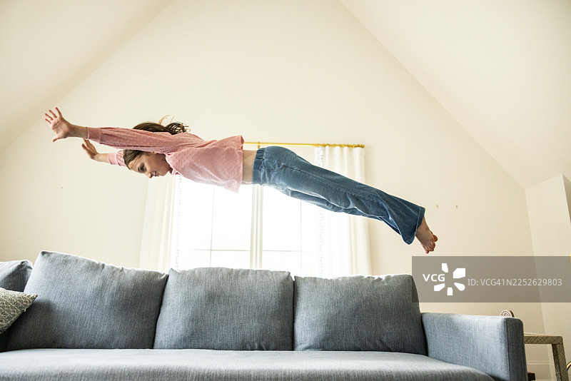 年轻女孩在家里的沙发上跳跃图片素材
