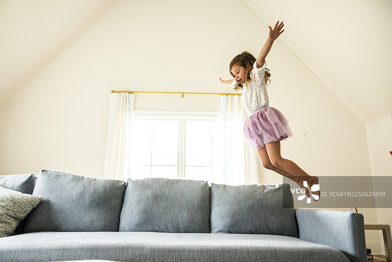 年轻女孩在家里的沙发上跳跃图片素材