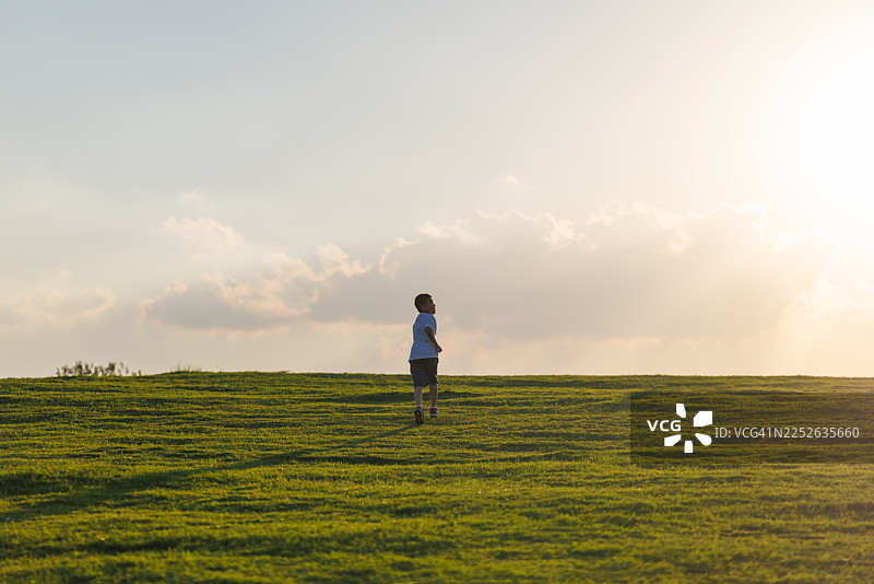 一个亚裔男孩在夕阳的余晖中，奔跑在地平线的草地上图片素材