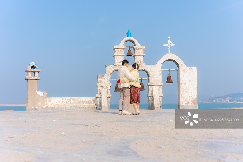 一对年轻夫妇在中国威海旅行，欣赏着标志性的白色钟楼的美景。图片素材