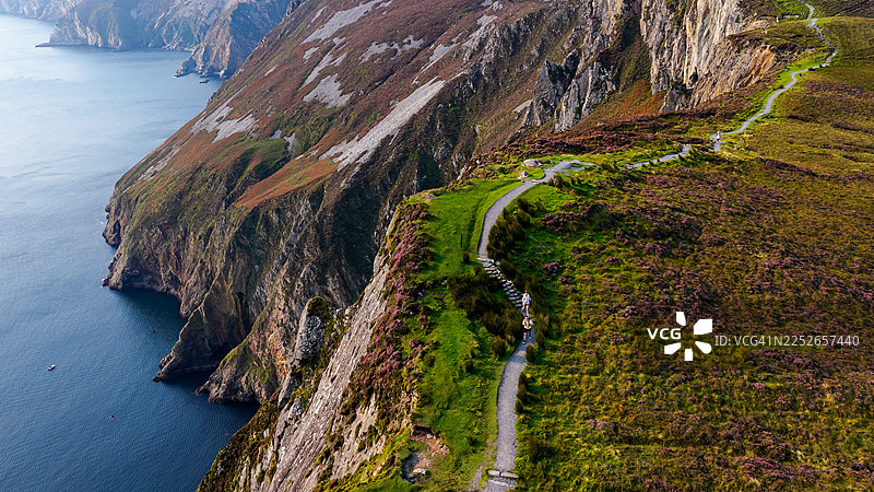 从空中俯瞰多尼戈尔郡斯莱夫利格陡峭悬崖旁的风景优美的徒步小径，遍布生机勃勃的石楠花，并可欣赏海岸全景，户外探险与爱尔兰自然旅行概念图片素材