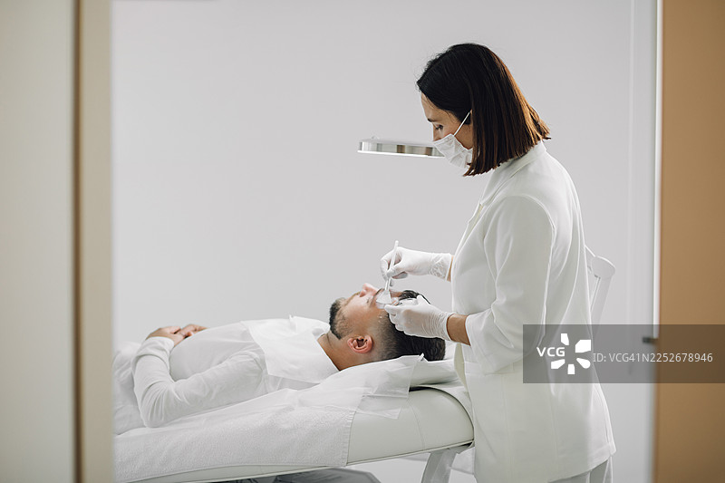 男士在健康水疗中心接受面部护理，女医生正在为他涂抹保湿霜或面部精华。图片素材