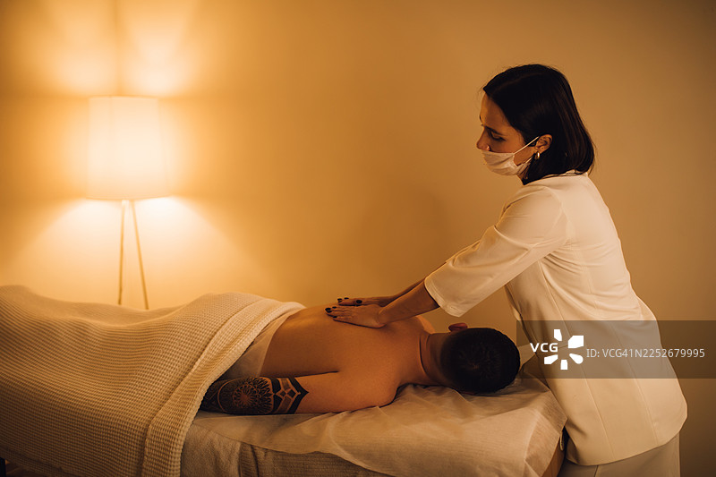 健康水疗中心男子接受背部按摩，氛围放松，灯光昏暗。图片素材