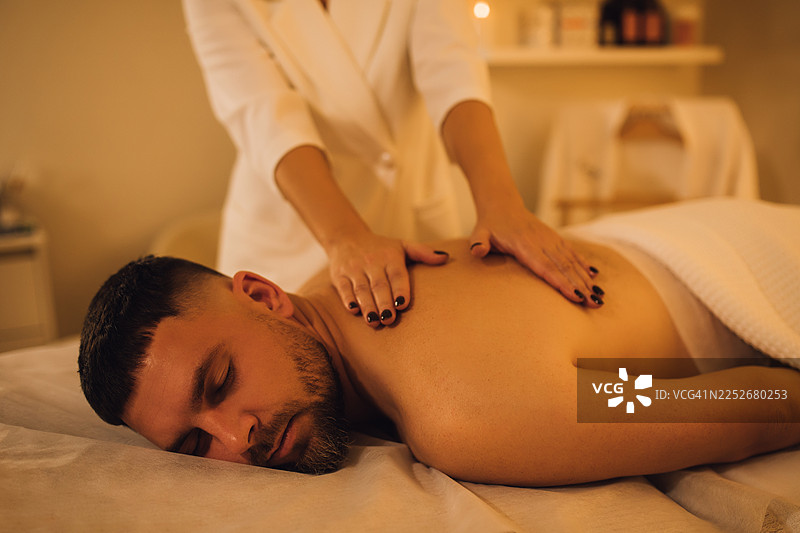 男士在健康水疗中心接受背部按摩，氛围放松，灯光昏暗。图片素材