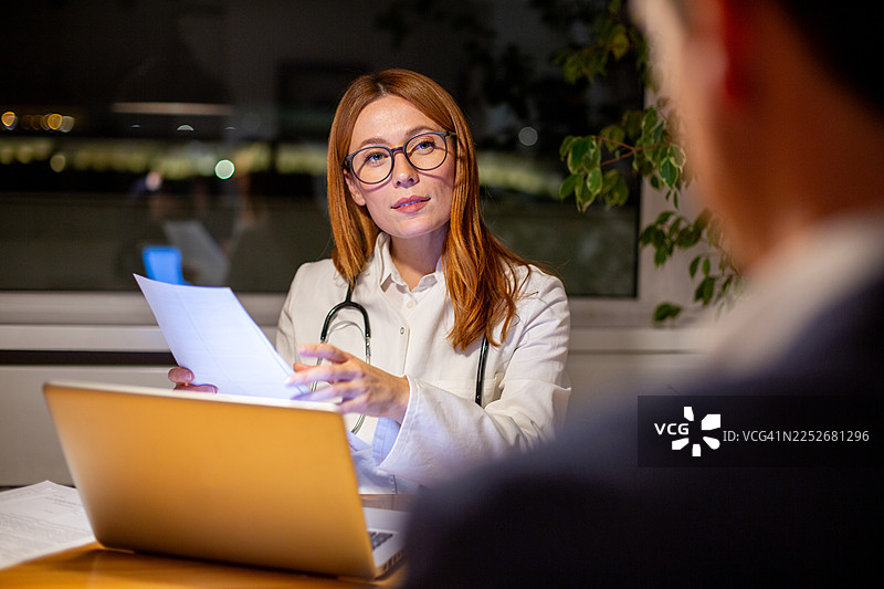 医生晚上在办公室向男病人解释医疗文件图片素材