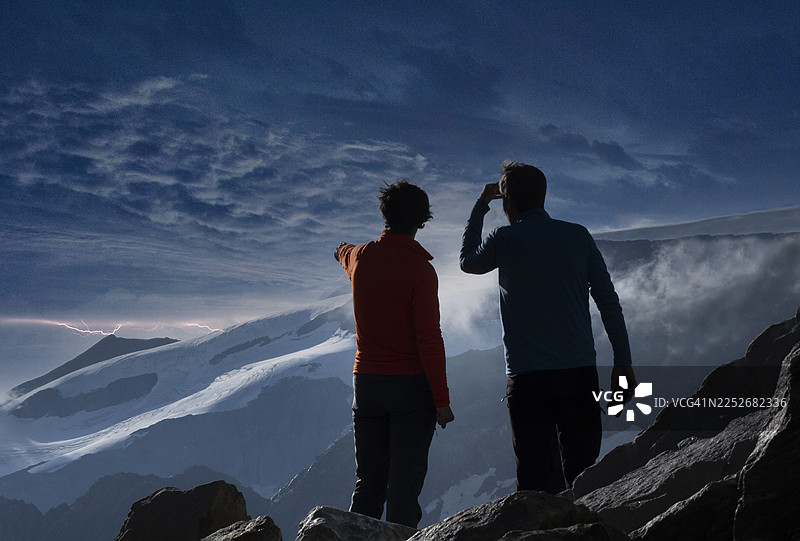 雷暴天气下，两位登山者正在观看山顶的闪电。图片素材