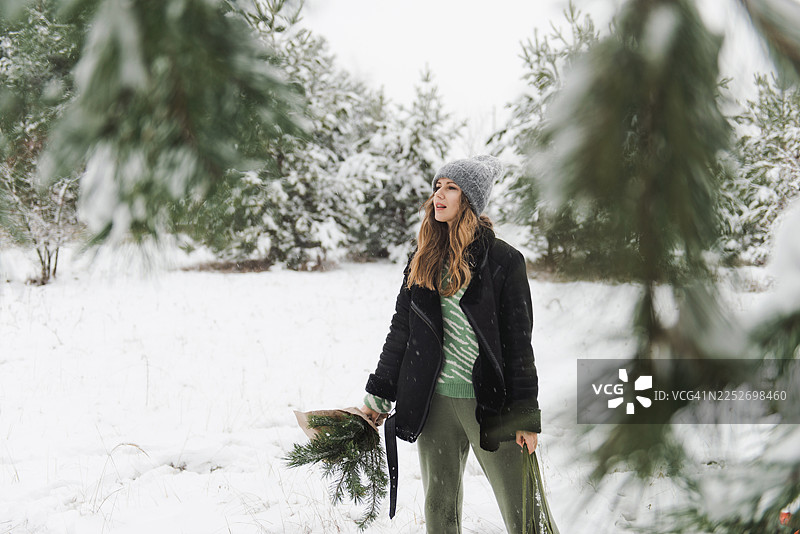 年轻女子身处白雪皑皑的森林中，四周环绕着被雪覆盖的树木和原始的冬日景观。图片素材