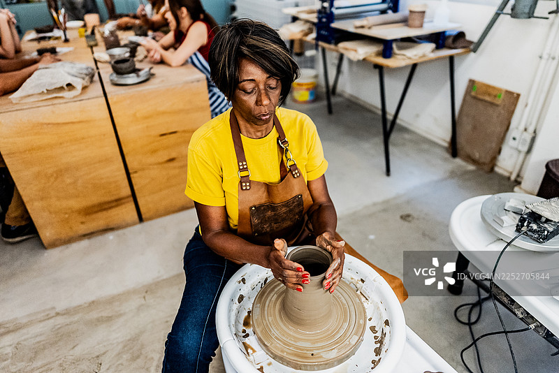 一位年长的女性在艺术工作室的陶轮上捏制陶土图片素材
