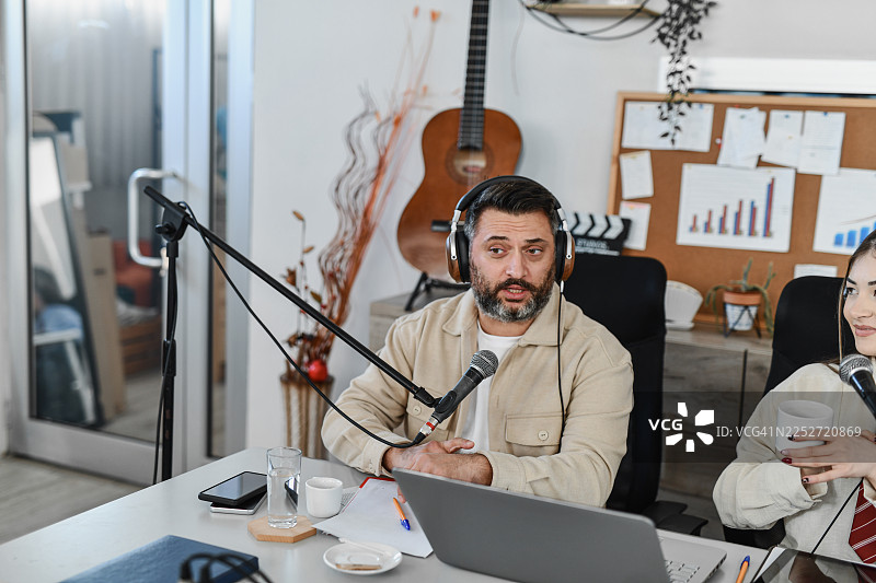 主播在现代录音棚里对着麦克风进行播客录音的抓拍场景图片素材