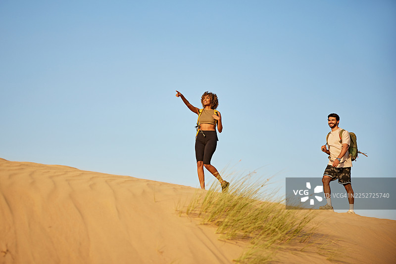 探险家们在沙漠沙丘上探索，一位女士指向远方的景色图片素材
