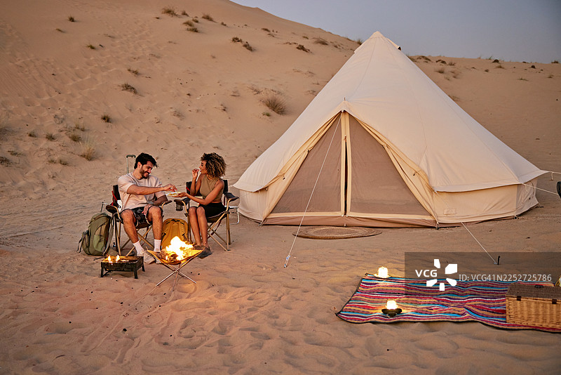 情侣在沙漠中露营，旁边有帐篷和营火图片素材