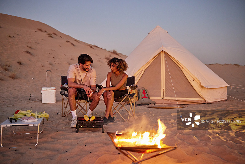 一对情侣在沙漠中露营，在帐篷附近烧烤做饭图片素材