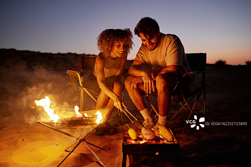情侣在沙漠夜晚露营，在篝火上烧烤图片素材