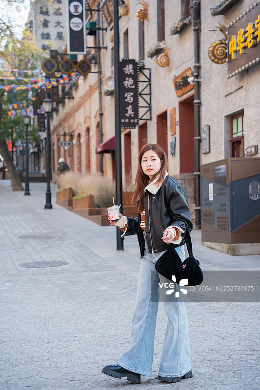 一位年轻女子在都市街道上漫步，同时使用智能手机图片素材