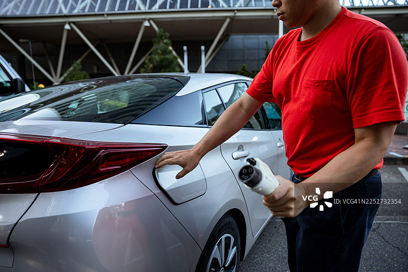 亚洲男性在城市充电站为电动汽车充电图片素材