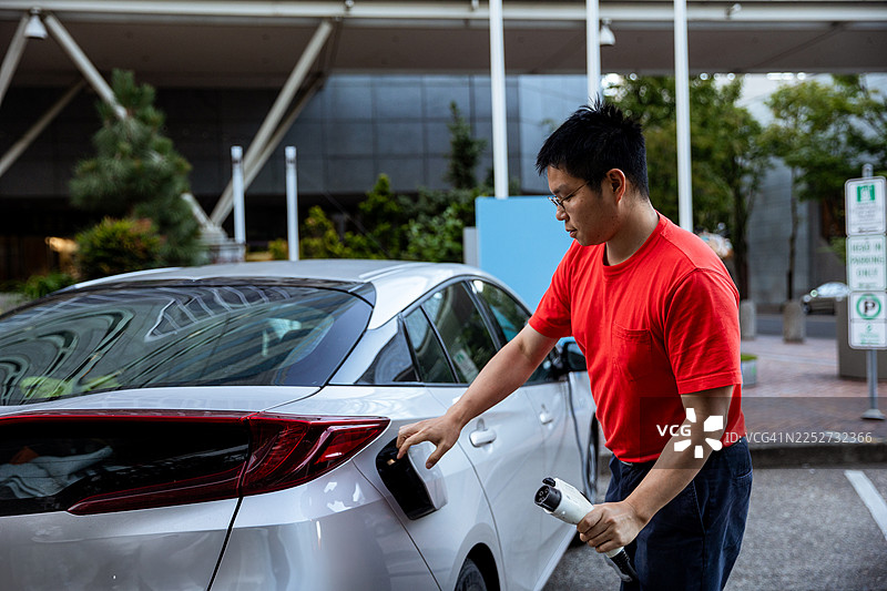 亚洲男性在城市充电站为电动汽车充电图片素材