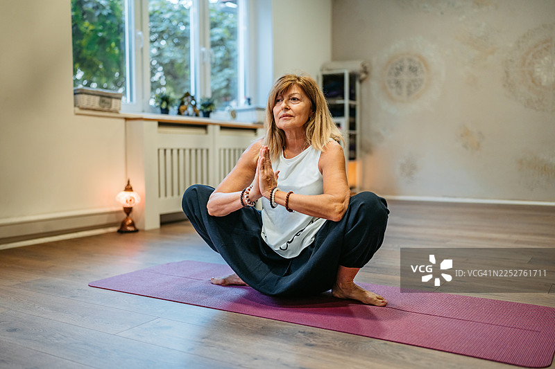 瑜伽室内，一位成熟的女性正在做花环式瑜伽图片素材