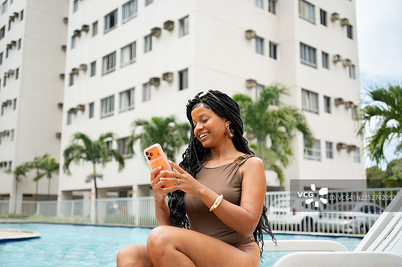 非洲裔女性在泳池边的躺椅上使用智能手机图片素材