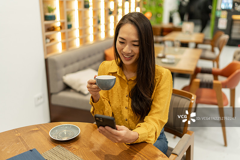 亚洲女子在咖啡馆里微笑着使用智能手机图片素材