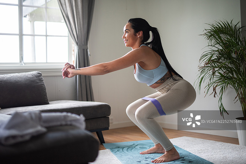 女子在家锻炼，使用弹力带进行深蹲。图片素材