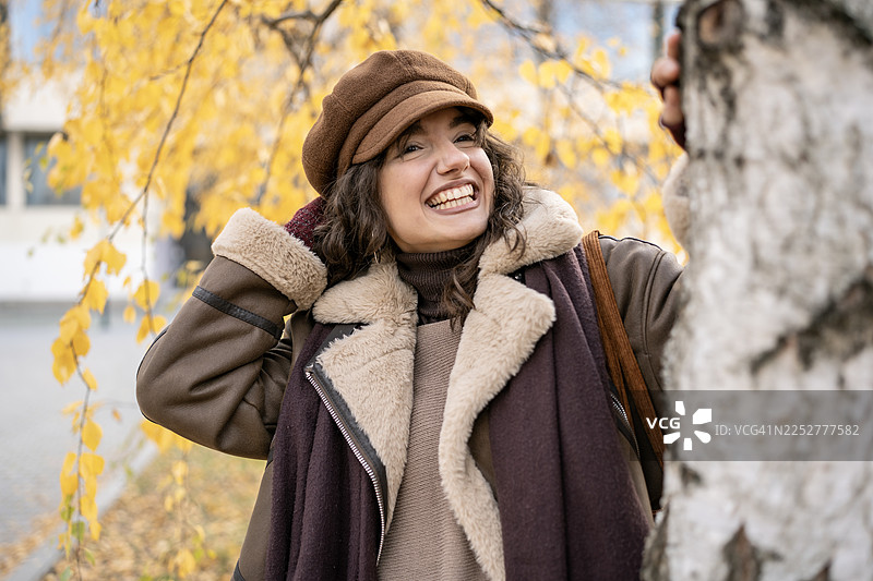 身穿舒适秋季外套的微笑女性在金黄落叶中享受户外秋日时光图片素材