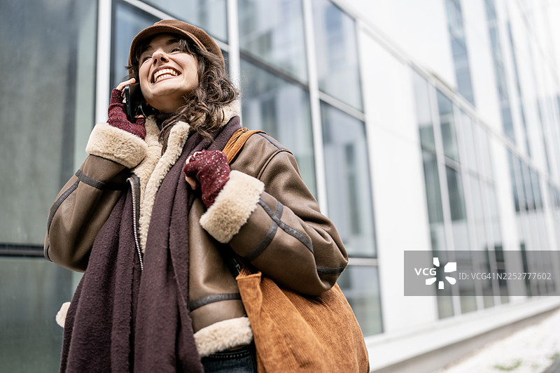 穿着暖和外套、围巾和手提包的快乐都市女性，在现代街道上接电话图片素材