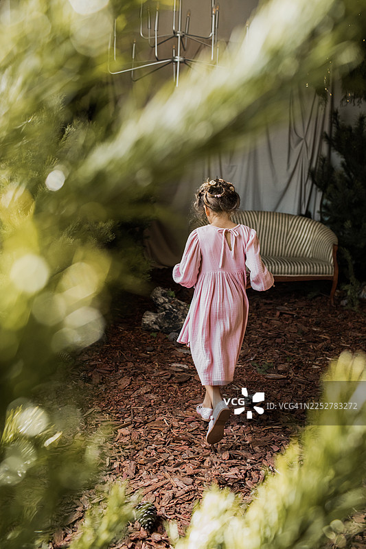 身穿粉色连衣裙的年轻女孩走在花园小径上，旁边有复古沙发和吊灯图片素材