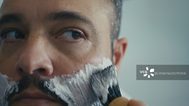 阳光透过窗户照进浴室，一位纹身男子正在刮胡子。图片素材