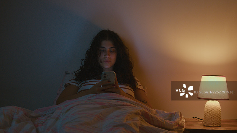 女子在床上黑暗中玩手机，手机光线映照在脸上图片素材