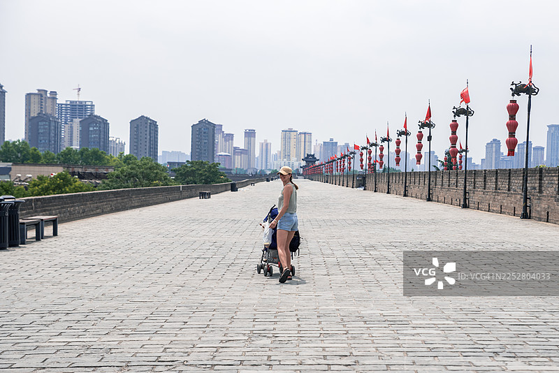 年轻的母亲微笑着推着婴儿车沿着西安城墙散步图片素材
