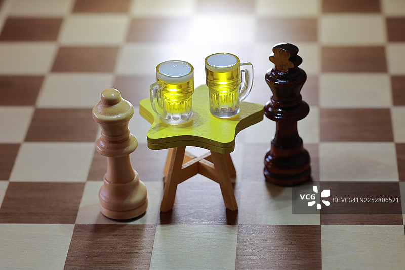 2026新年国际象棋主题。一场王者对决。一个黑方国王和一个白方王后国际象棋棋子，坐在一张小小的黄色星形桌子两边，每人面前都放着一个迷你啤酒杯。图片素材