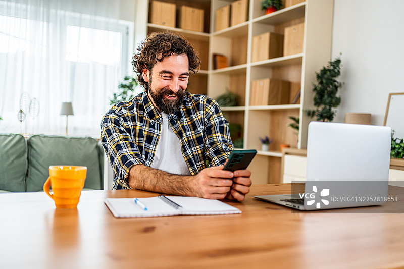 面带微笑的男士在家中使用智能手机工作图片素材