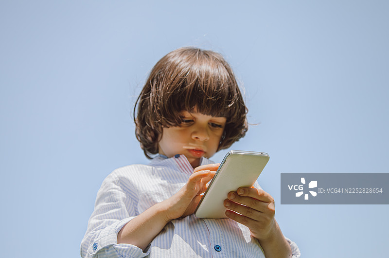 一个穿着阿拉伯服饰的小男孩，在阿联酋迪拜的绿色公园里，一边使用智能手机一边打电话。图片素材