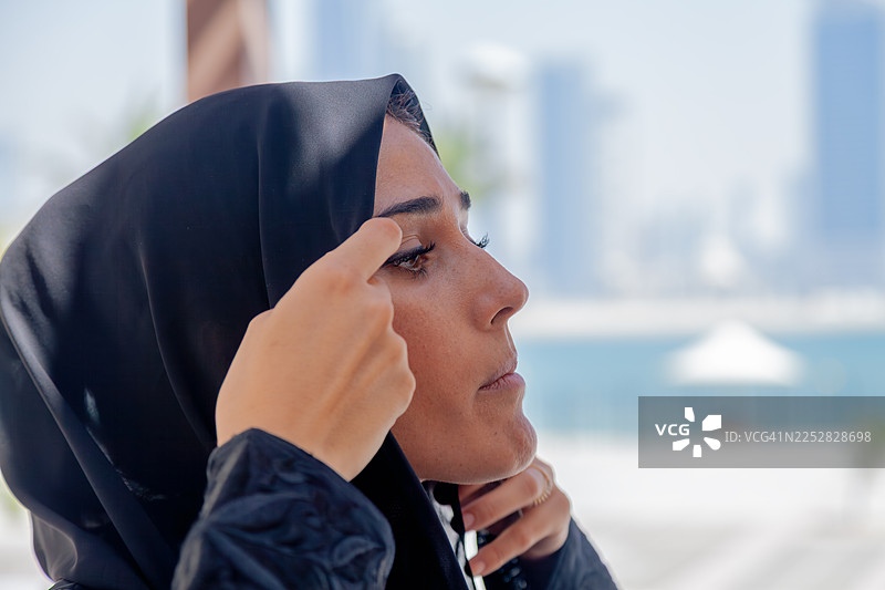 一位阿拉伯女商人在现代迪拜城市天际线背景下，在户外调整她的希贾布。图片素材