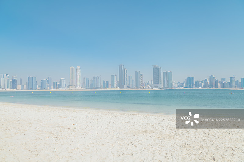 在蔚蓝天空下，广阔的迪拜天际线横跨碧绿海水和白色沙滩，呈现出宽幅全景视图图片素材