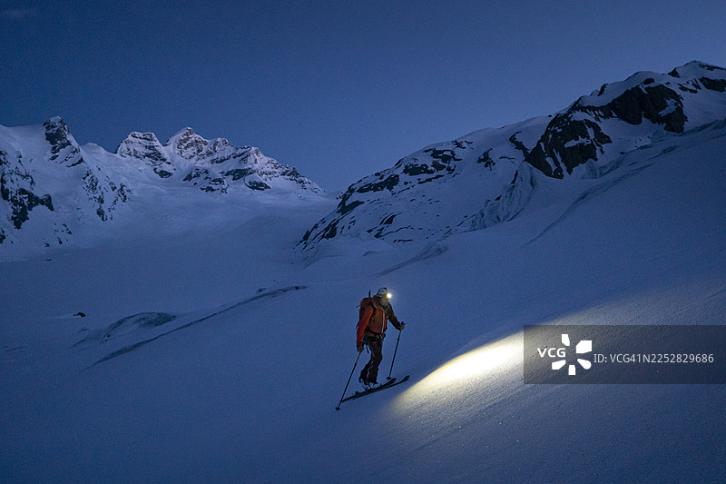 黄昏时分，一名高山滑雪登山者正在攀登积雪的山脊。图片素材