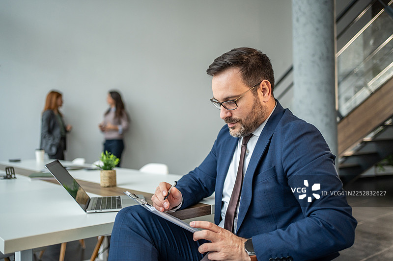 专注的商人在办公室会议中在文件板上书写图片素材