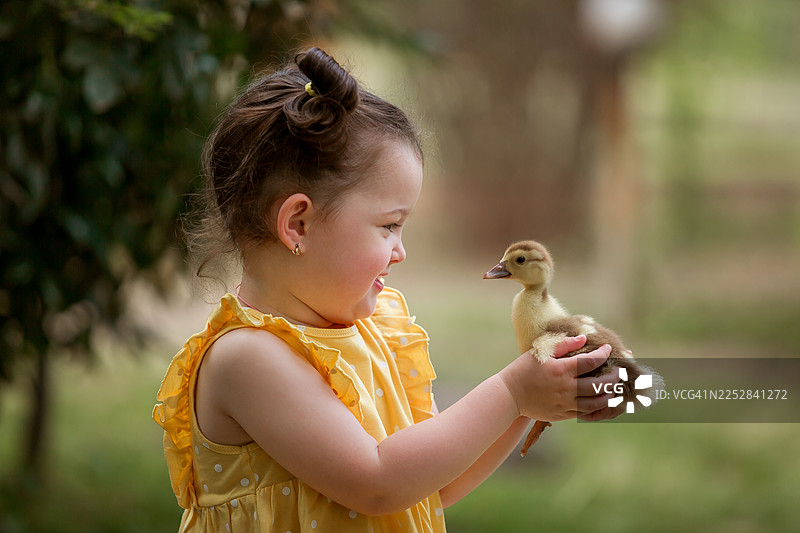 小女孩在花园里抱着一只小鸭子。图片素材