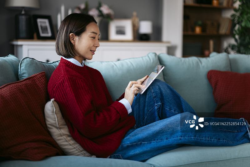 亚洲女性舒适地躺在沙发上使用平板电脑图片素材