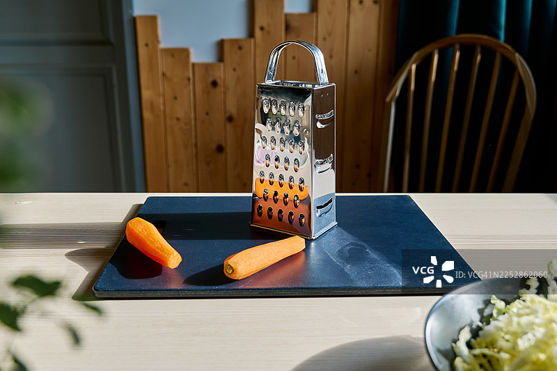 切菜板上放着胡萝卜、擦丝器和一碗切好的北京白菜。烹饪健康食品。图片素材