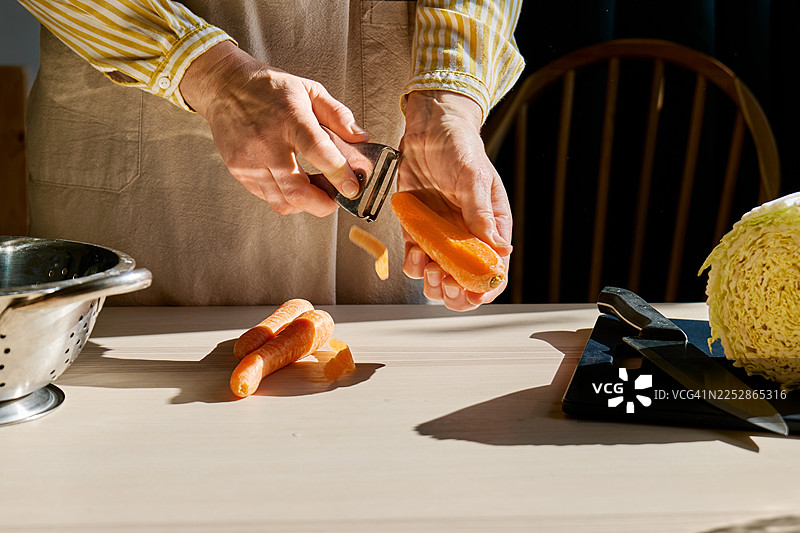 穿着围裙的陌生女子用削皮器削胡萝卜的手图片素材