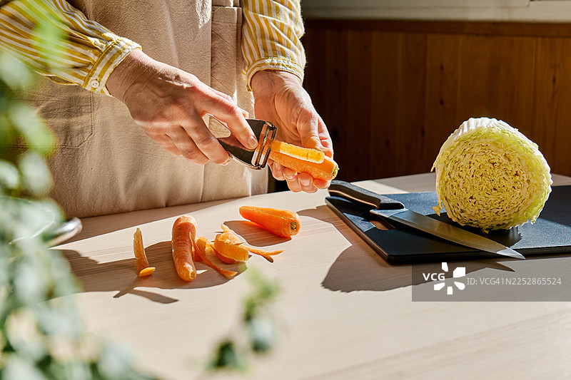 围裙里一位无法辨认的女性正在用削皮器削胡萝卜。图片素材