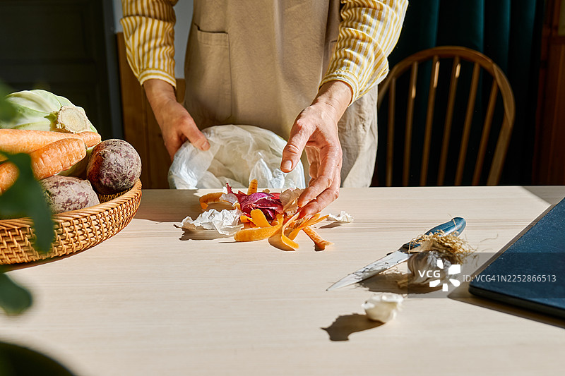 一位不知名女子在家将胡萝卜和洋葱的蔬菜皮扔进垃圾桶。图片素材