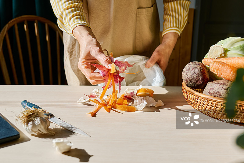 一位身份不明的女士在家将胡萝卜和洋葱的菜皮扔进垃圾桶。图片素材
