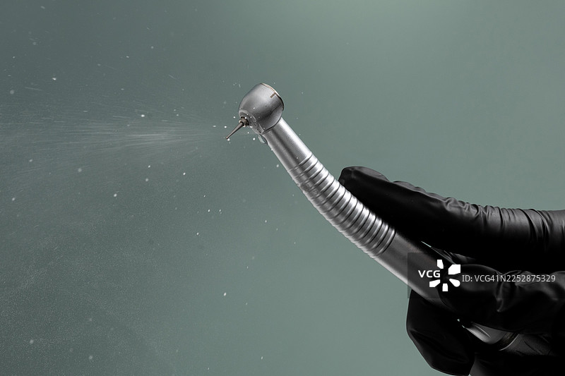 牙医在操作过程中使用高速牙科手机喷水，手持工具，戴着黑色手套。图片素材