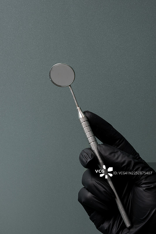 戴着黑色手套的手，手持牙科镜，背景为灰色，用于展示牙科健康与卫生概念图片素材