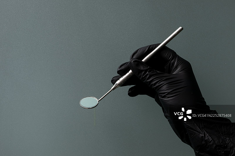 戴着黑色手套的手握着牙科镜，阐释牙齿护理和口腔卫生的概念图片素材