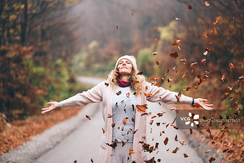 身着舒适秋装的快乐女子在小径上抛洒秋叶图片素材